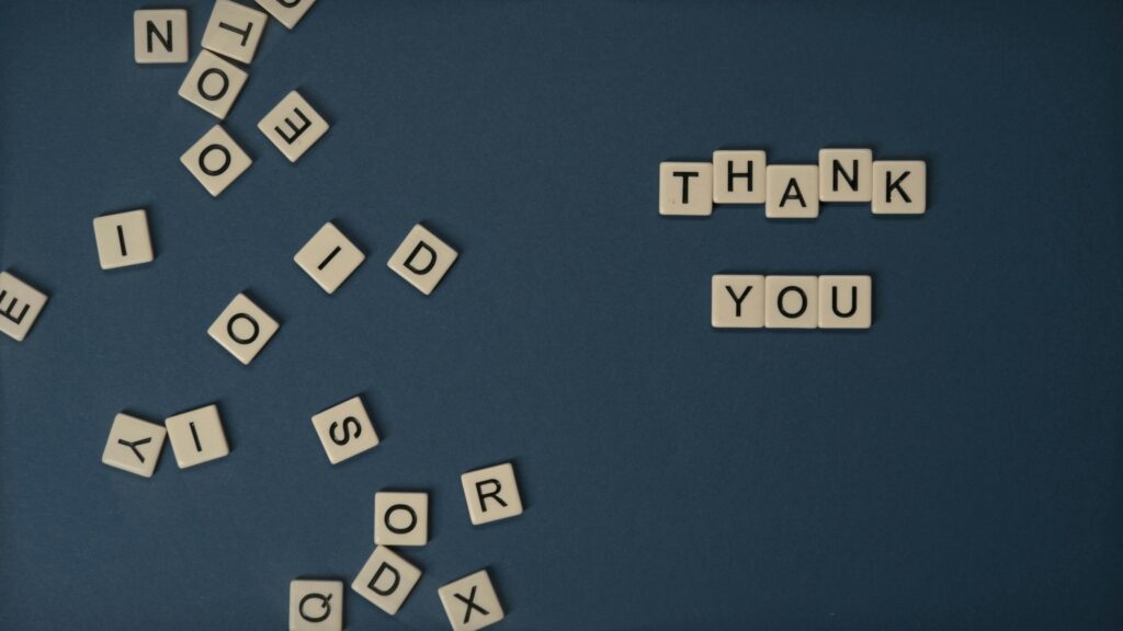 Top view of scattered Scrabble tiles with Thank You spelled out on blue surface.